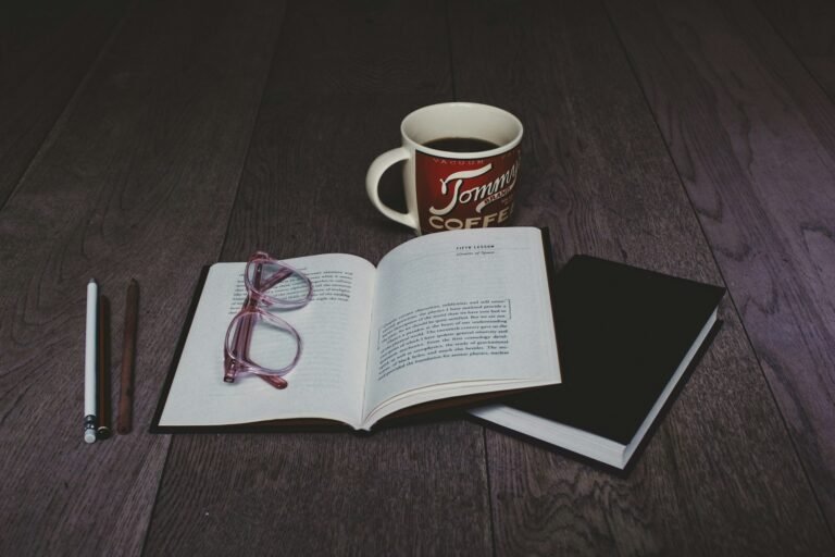 Livros que mudam a vida: livro aberto com óculos, caderno e caneca de café sobre a mesa