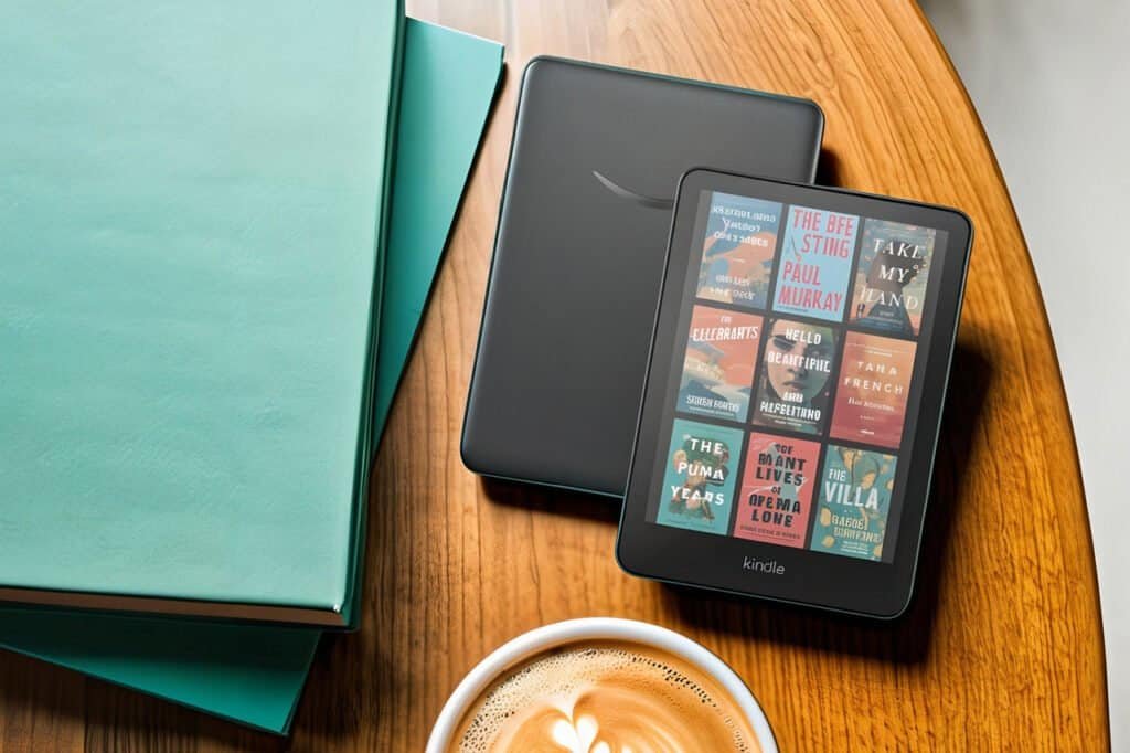 Kindle Colorsoft com capas coloridas na tela ao lado de um Kindle Paperwhite sobre mesa de madeira