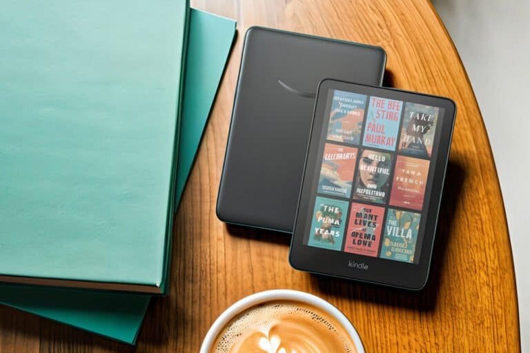 Kindle Colorsoft com capas coloridas na tela ao lado de um Kindle Paperwhite sobre mesa de madeira