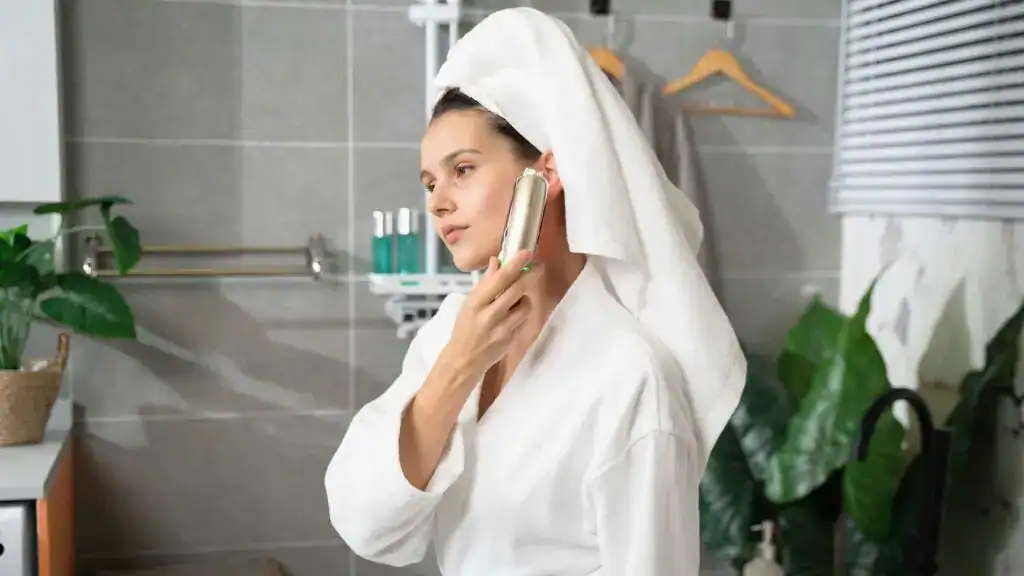 Mulher de roupão aplicando produto no rosto no banheiro