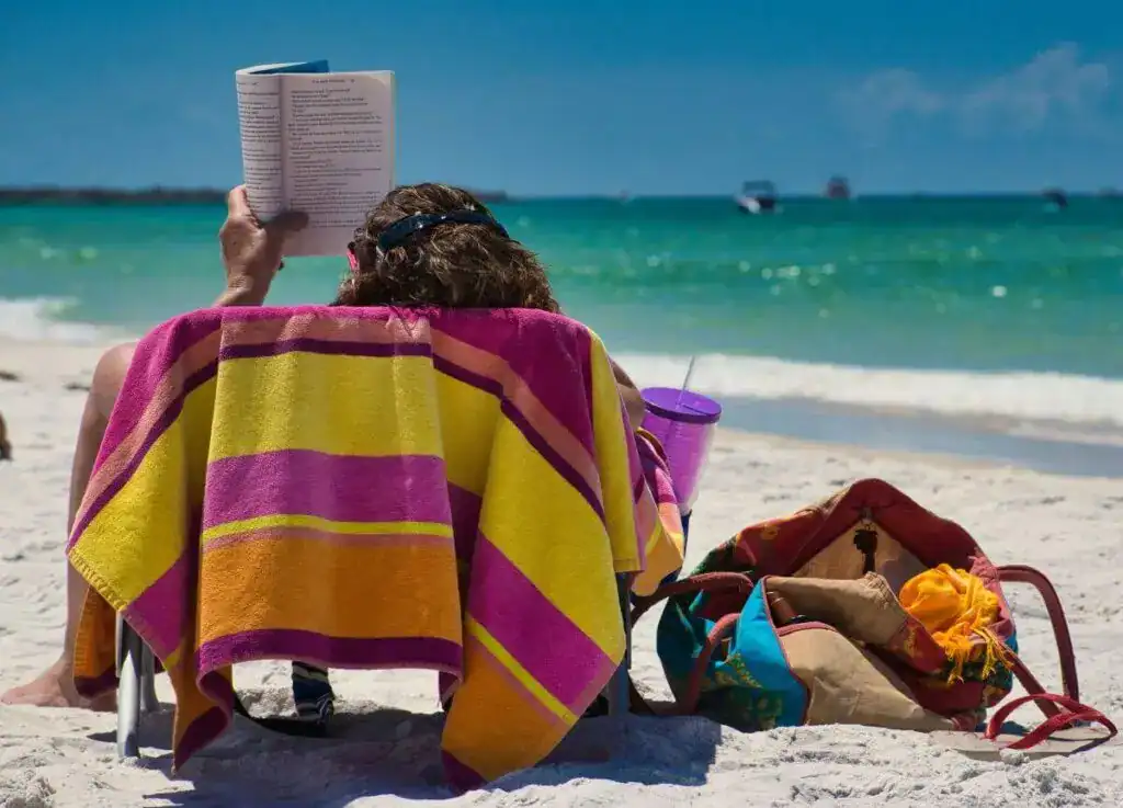 Mulher lendo na praia com bolsa de itens essenciais para proteção solar e hidratação no Nordeste